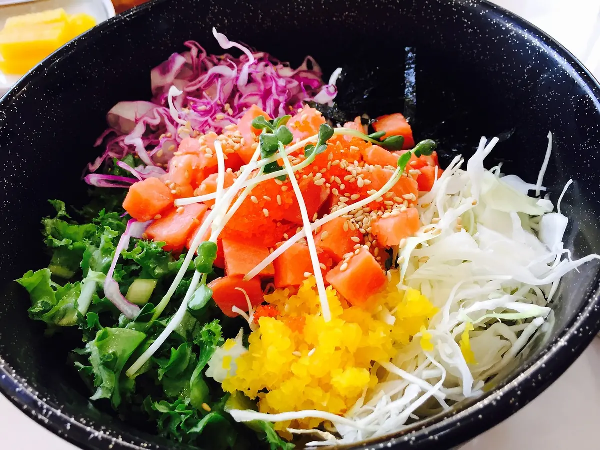 Bowl of rice topped with diced raw salmon, shredded cabbage, greens and sesame seeds