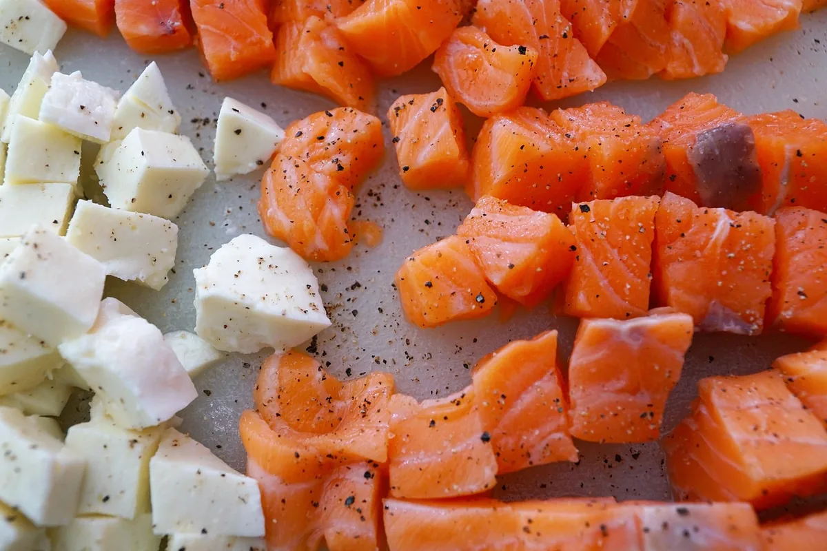Raw salmon cut into bite-size cubes on a board, with cubes of cheese beside them