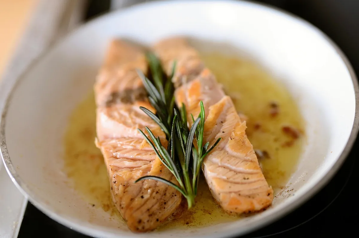 Pieces of salmon cooking in a pan with butter and a sprig of rosemary