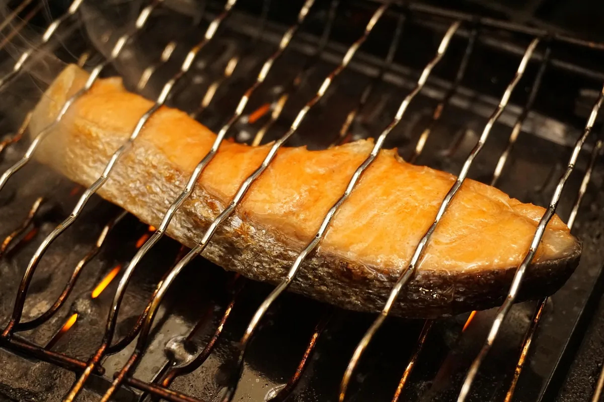 Salmon fillet cooking on a hot grill grate over glowing coals