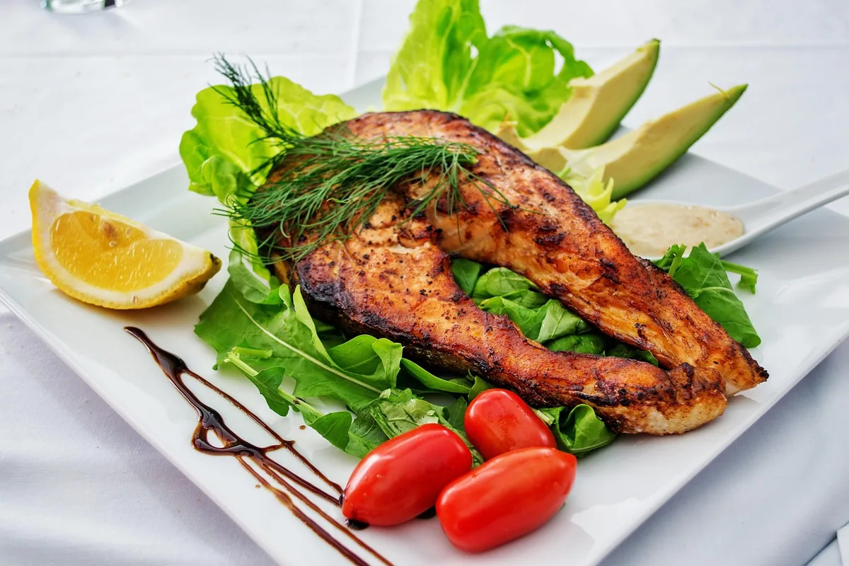 Grilled salmon steak with dill, lettuce, avocado, cherry tomatoes and a lemon wedge