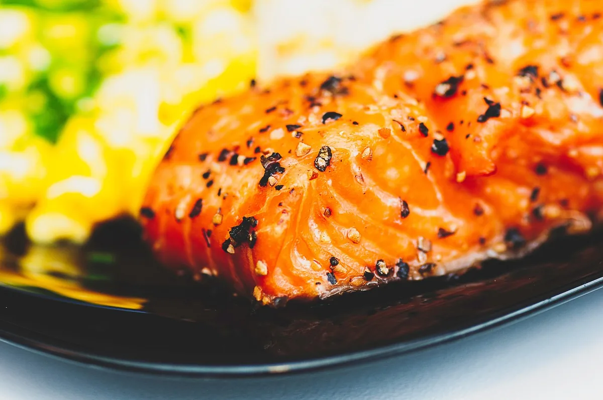 Close-up of a glazed salmon fillet with cracked pepper on a dark plate