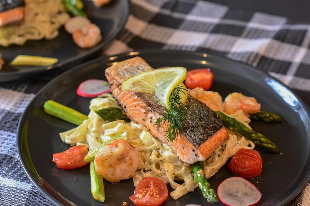 Seared salmon fillet with lemon and dill served over pasta with asparagus and tomatoes