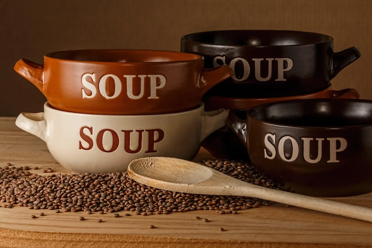 Three soup bowls on a wooden board with dry brown lentils and a wooden spoon
