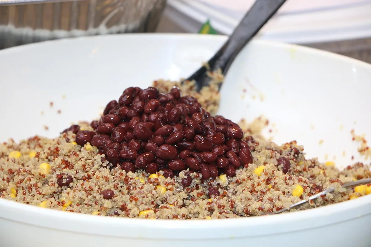 Cooked quinoa with black beans and corn being mixed in a white bowl