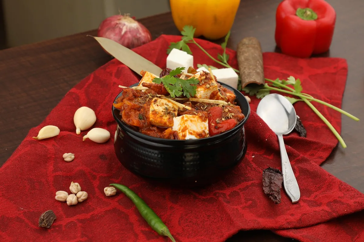 Paneer cubes in a spicy tomato gravy in a black bowl, garnished with cilantro