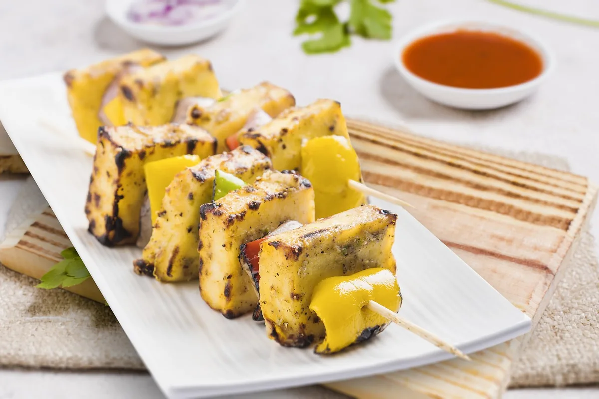 Grilled paneer tikka skewers with yellow bell pepper and a small bowl of sauce