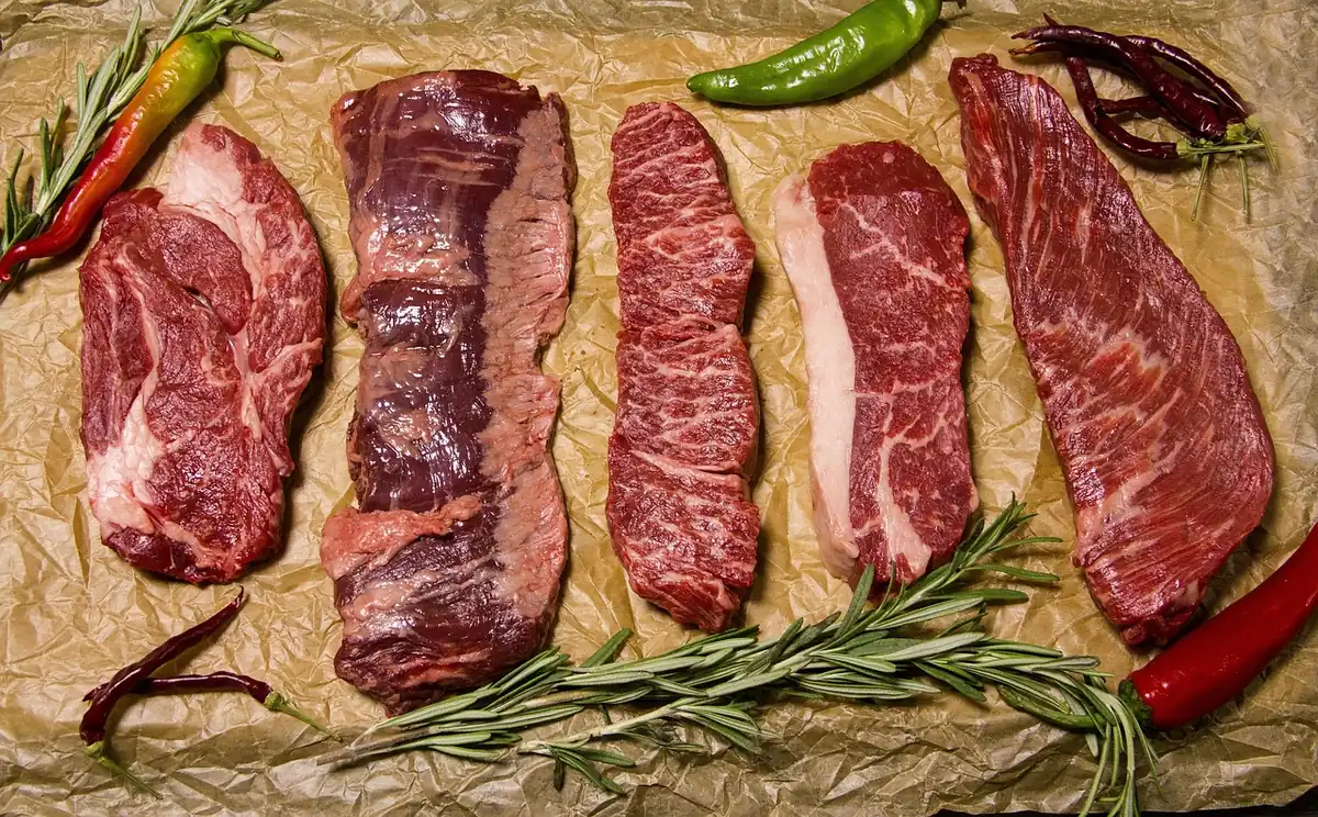 Five raw beef steak cuts on brown paper with rosemary and chili peppers, ready for traeger recipes steak
